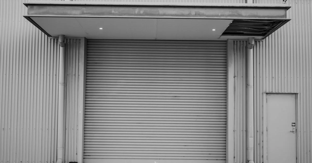 Image en noir et blanc d'une porte de garage industrielle fermée avec un extérieur en métal ondulé.