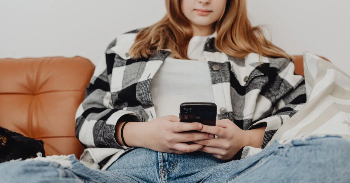 Fille adolescente assise sur le canapé, absorbée par son smartphone, montrant un style de vie détendu.
