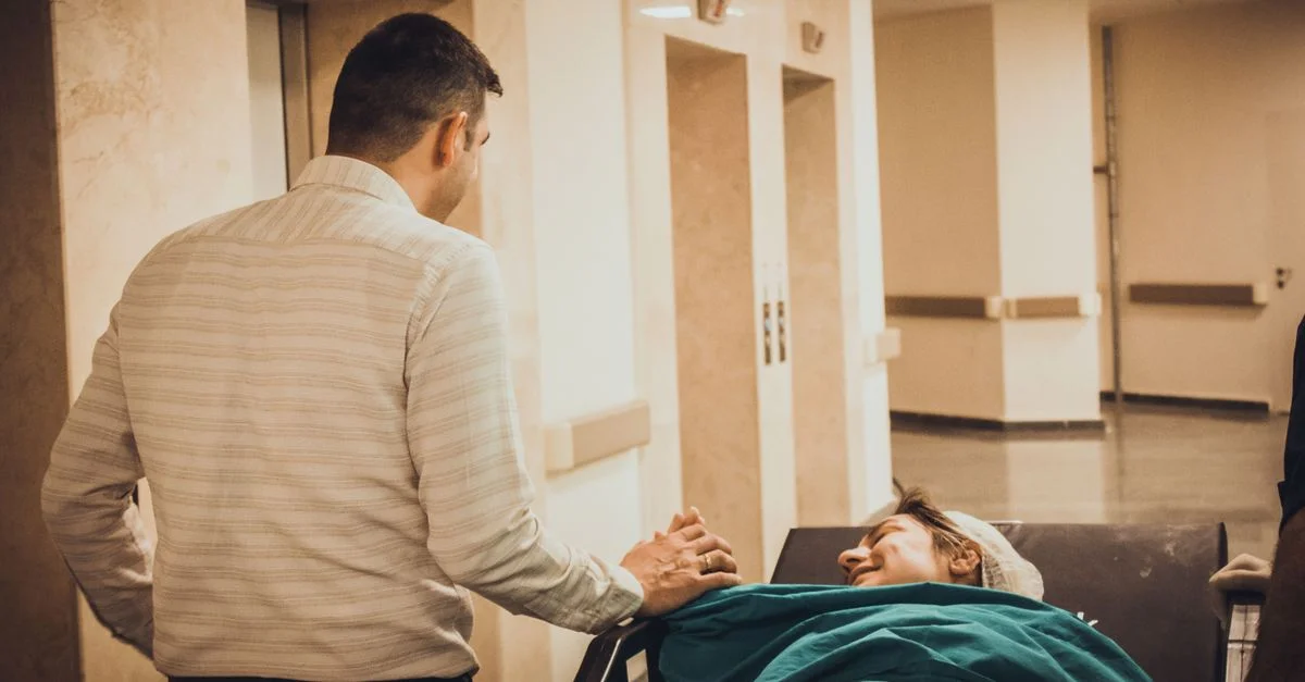Un homme réconforte une patiente sur une civière dans un couloir d'hôpital, transmettant un sentiment de soin et de soutien.