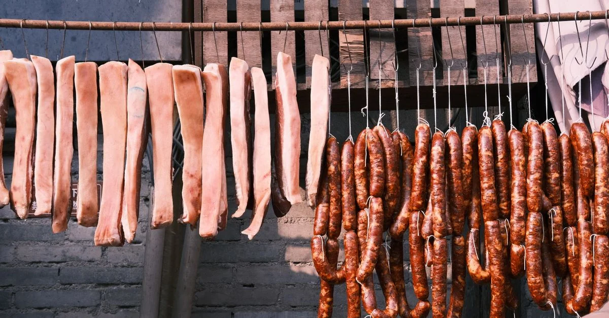 Des morceaux de viande crue et des saucisses séchant en plein air, mettant en avant des méthodes traditionnelles de conservation des aliments.
