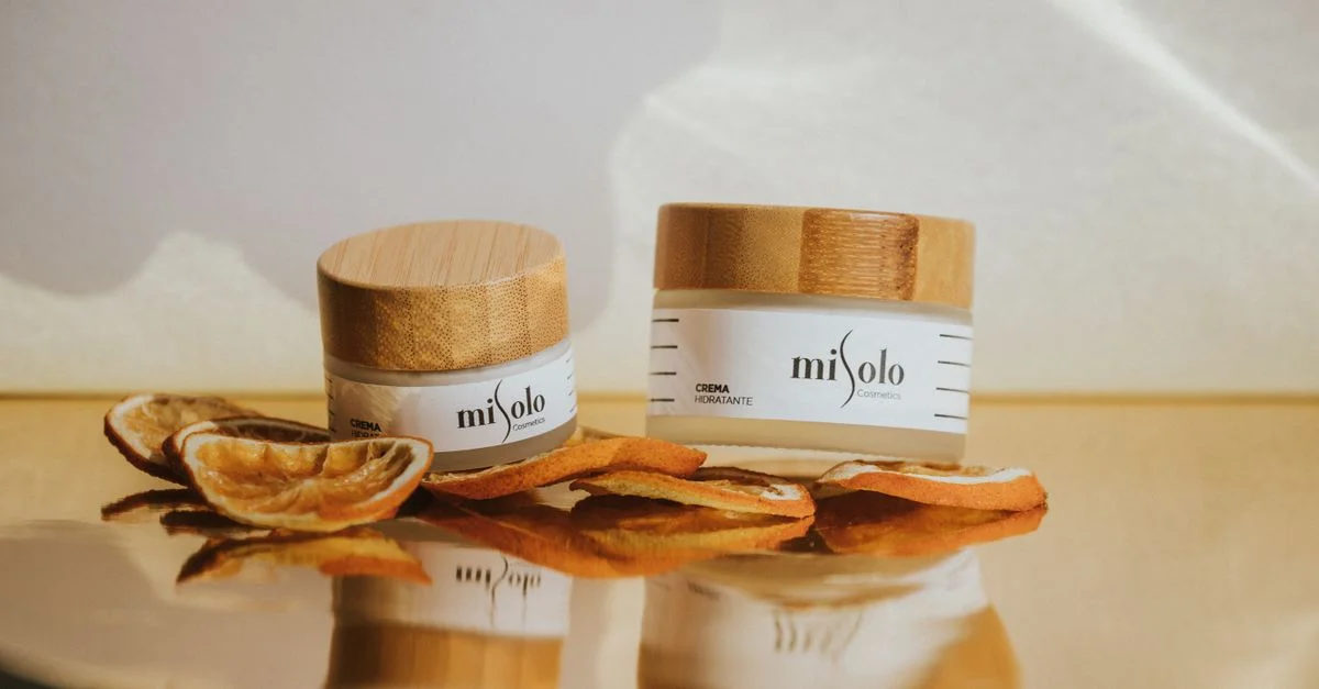 Jars de crème hydratante avec des couvercles en bambou naturel, accentués par des tranches d'orange séchées.