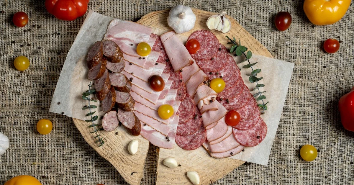 Une vue en plongée de viandes séchées assorties et de tomates fraîches sur une planche en bois rustique.