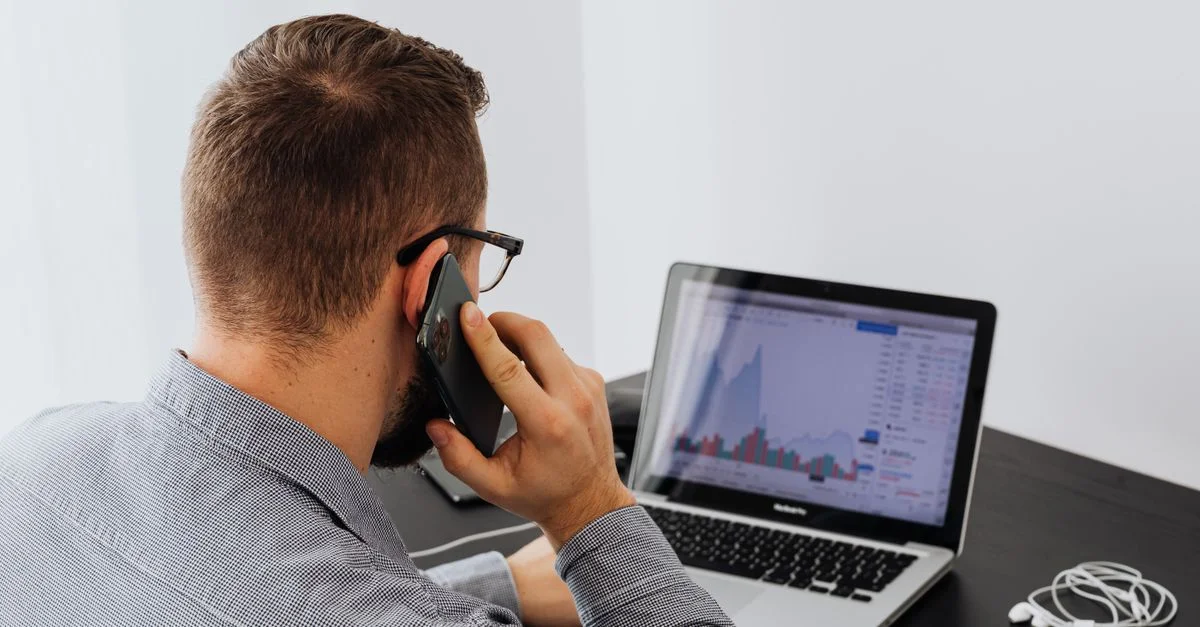 Un homme d'affaires analyse des données boursières sur un ordinateur portable tout en parlant au téléphone à son bureau.