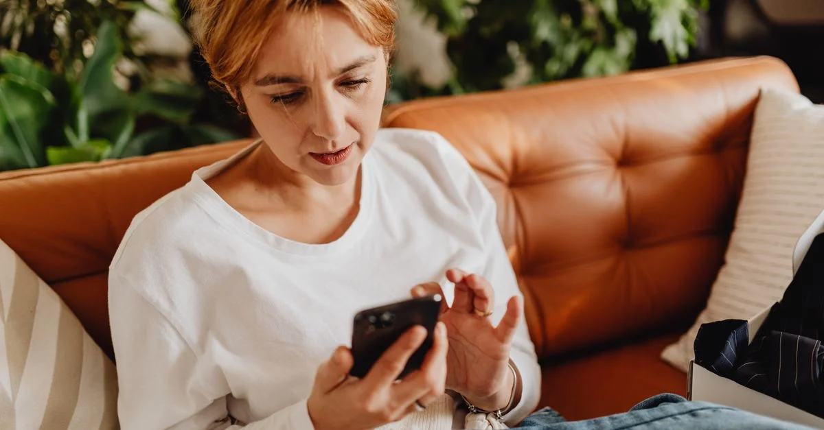 Femme en tenue décontractée utilisant un smartphone sur un canapé confortable entouré de plantes.