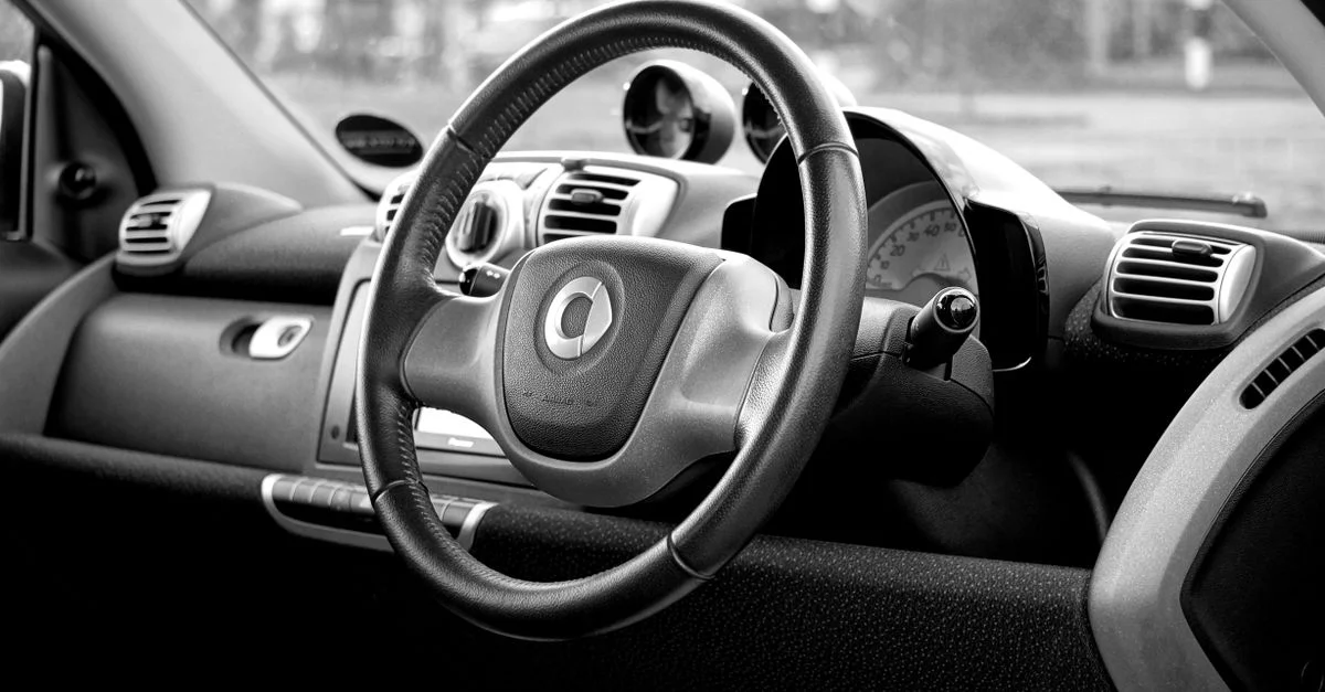 Photo en noir et blanc de l'intérieur d'une voiture intelligente présentant un tableau de bord moderne et un volant.