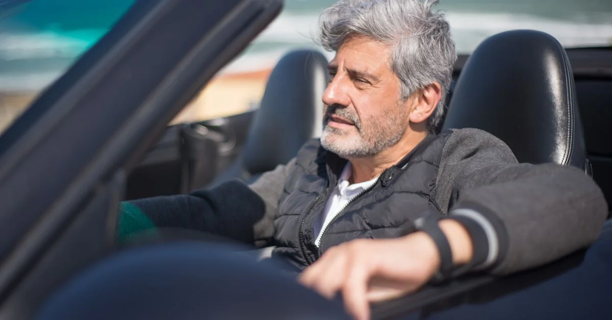 Un homme senior profitant d'un road trip le long d'une route côtière pittoresque dans une voiture décapotable.