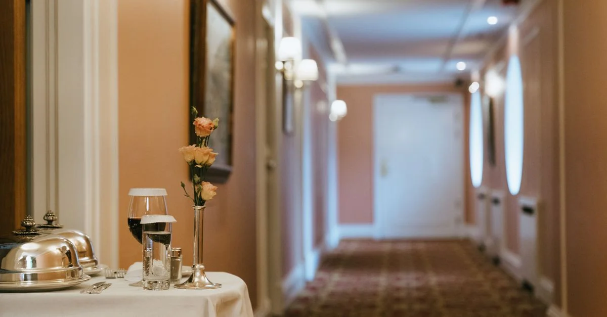 Un couloir d'hôtel luxueux avec une table de service en chambre ornée de fleurs et de vin, créant une ambiance chaleureuse.