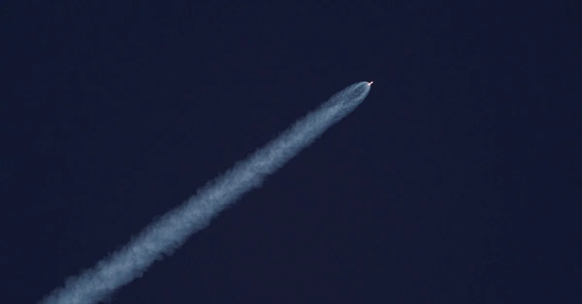 Une fusée s'élève dans le ciel, laissant une traînée de fumée contre le ciel bleu clair.